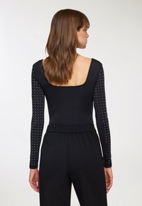 Body nero con maniche lunghe, caratterizzato da uno scollo quadrato e decorazioni a pois lungo le maniche. Tessuto morbido con una silhouette aderente.