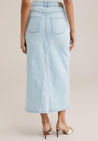 Fustă din denim albastru deschis, cu talie ajustată, două buzunare posteriori și croială dreaptă. Are o cusătură centrală și un tiv puțin sub genunchi.