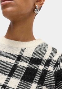 Sweter w kratę w czarno-białej wełnie z okrągłym dekoltem. Posiada teksturowany wzór i gładką, błyszczącą, srebrną powiewkę w kształcie kuli.