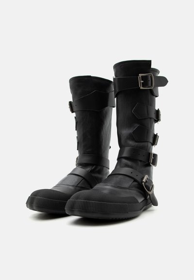 Ψηλές μαύρες δερμάτινες μπότες με πολλαπλές ρυθμιζόμενες αγκράφες και λαστιχένιες σόλες, φωτογραφημένες σε απλό λευκό φόντο.