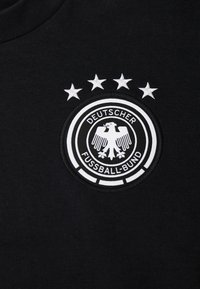 Svart stoff med Deutscher Fussball-Bund-logoet som har en hvit ørn inni en sirkel og fire hvite stjerner over.