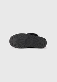 Svart gummisåle med et teksturert mønster, som har spor og rygger for godt grep. Holdbart materiale designet for stabilitet og grep.