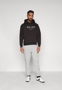 Felpa nera con stampa grafica, tasca frontale e orlo a coste; abbinata a pantaloni jogger grigi chiari e sneaker bianche. Design semplice e informale.