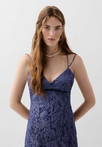Navyblaues Kleid mit strukturiertem Tierdruck, Spaghettiträgern und V-Ausschnitt. Glatter Stoff mit taillierter Silhouette. Akzent mit Perlenkette.