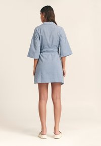 Plava i bijela karirana haljina s vezanim strukom, kratkim kimono rukavima i opuštenim krojem, izrađena od lagane tkanine.