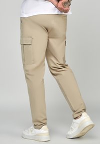 Beiga cargobyxor med sidfickor, tillverkade av ett slätt material. Bärs med vita sneakers som har en subtil design och texturerade detaljer.