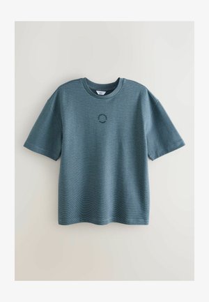 Rövid ujjú, kék póló, puha anyagból, bordázott textúrával és középen elhelyezett kis kör alakú logóval.