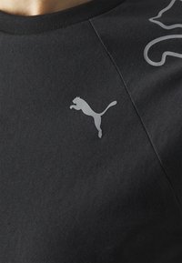 Camiseta de algodón negra de manga corta, con un logotipo gris de Puma en el lado izquierdo y una textura suave y mate.