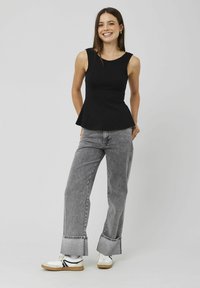 Top peplum noir avec un col rond, un buste ajusté et un ourlet évasé. Associé à un jean large gris et des baskets blanches.