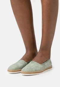 Ljust gröna espadriller i mjukt tyg, med rund tåsko, vävd jutesula och dekorativ sömnad längs kanten.