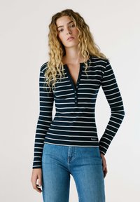 Námořnický a bílý pruhovaný top s dlouhými rukávy, s výstřihem henley, s knoflíkovými detaily a přiléhavým střihem, v kombinaci s modrými džíny.