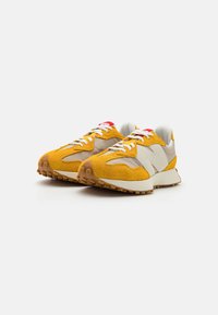Yellow suede and beige fabric sneakers with light-colored soles, featuring white laces and red accents on the tongue.