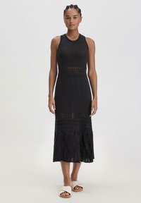 Abito midi nero in maglia con corpo aderente, dettagli in pizzo e orlo svasato, abbinato a sandali beige a scivolo.