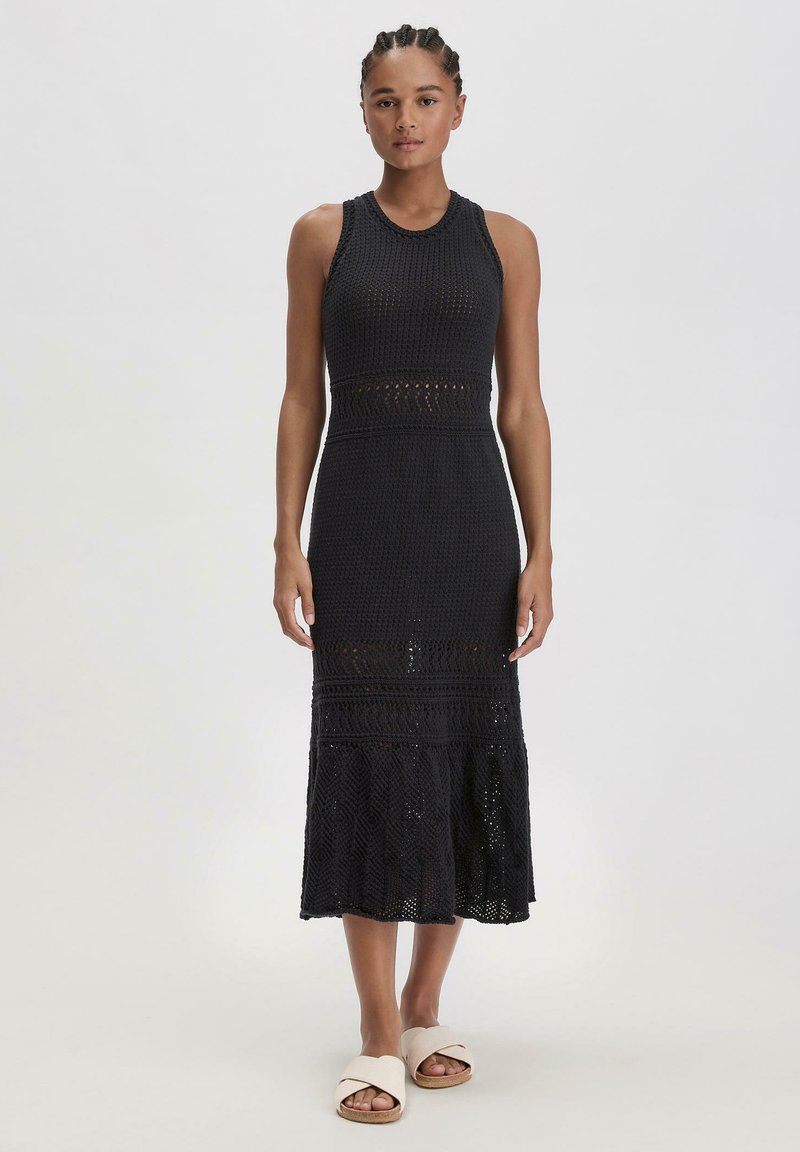 Abito midi nero in maglia con corpo aderente, dettagli in pizzo e orlo svasato, abbinato a sandali beige a scivolo.