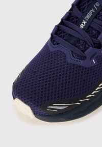 Close-up van een marineblauwe sportschoen met een bovenwerk van mesh, veters en de tekst "RX DEFY" op de tongtab, waarbij voor- en zijdetails worden getoond.