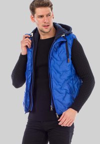 Blauer Puffer-Weste mit Kapuze, ausgestattet mit einer gesteppten Textur und einem kontrastierenden marineblauen Innenfutter. Mit Reißverschlusstaschen und verstellbaren Kordeln.