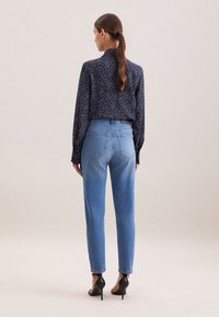 Top blu navy con pois bianchi, scollatura alta e maniche lunghe, abbinato a jeans a vita alta blu chiaro e sandali neri con tacco.