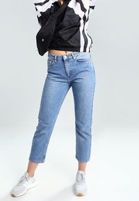 Ljusblå, korta denimjeans med rak benpassform, med en klassisk femfickdesign. Bärs med en svart och vit jacka och vita sneakers.