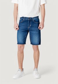 Shorts de denim en azul oscuro, con un clásico diseño de cinco bolsillos, dobladillo deshilachado y una textura suave. Combinados con zapatillas blancas.