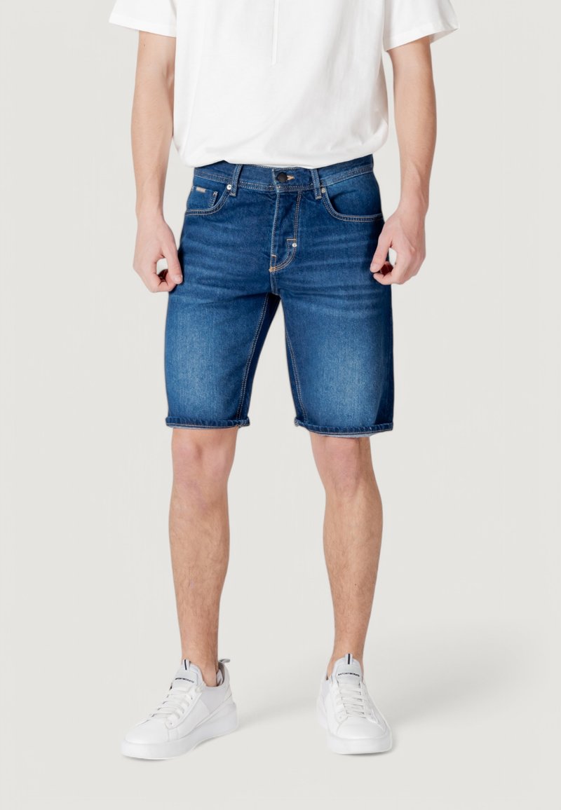 Shorts de denim en azul oscuro, con un clásico diseño de cinco bolsillos, dobladillo deshilachado y una textura suave. Combinados con zapatillas blancas.