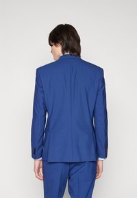 Blå skräddarsydd kavaj med klassisk notch-lapel, enkel slits och knappade ärmar. Tyget har en subtil struktur.