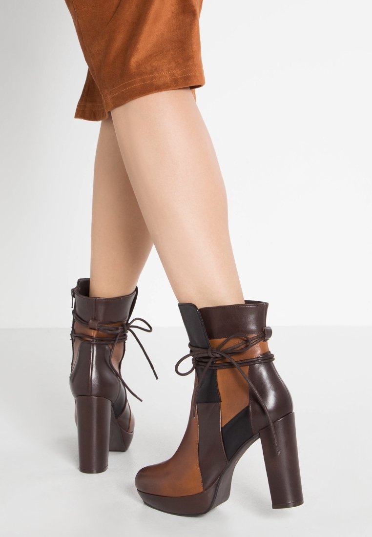 Vrouw in bruin en zwart hoge hakken enkelboots met veters en plateauzolen, gecombineerd met een roestkleurige rok of korte broek.