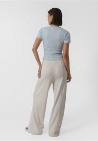 Haut à manches courtes côtelé bleu clair associé à un pantalon large crème, avec une texture lisse et des détails de couture centrale.