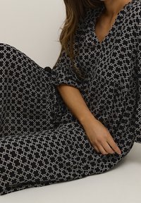 Vestido de estampado en blanco y negro con un diseño geométrico, mangas cortas, escote en V y detalle de cintura fruncida.