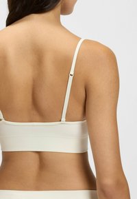 Bralette de couleur crème avec des bretelles ajustables, design sans coutures et texture de tissu douce, mettant en valeur une silhouette lisse au dos.