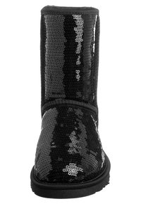 Botín negro con lentejuelas, puntera redondeada, forro de tela suave y suela plana de goma. Presenta una parte superior lisa y detalles de lentejuelas.