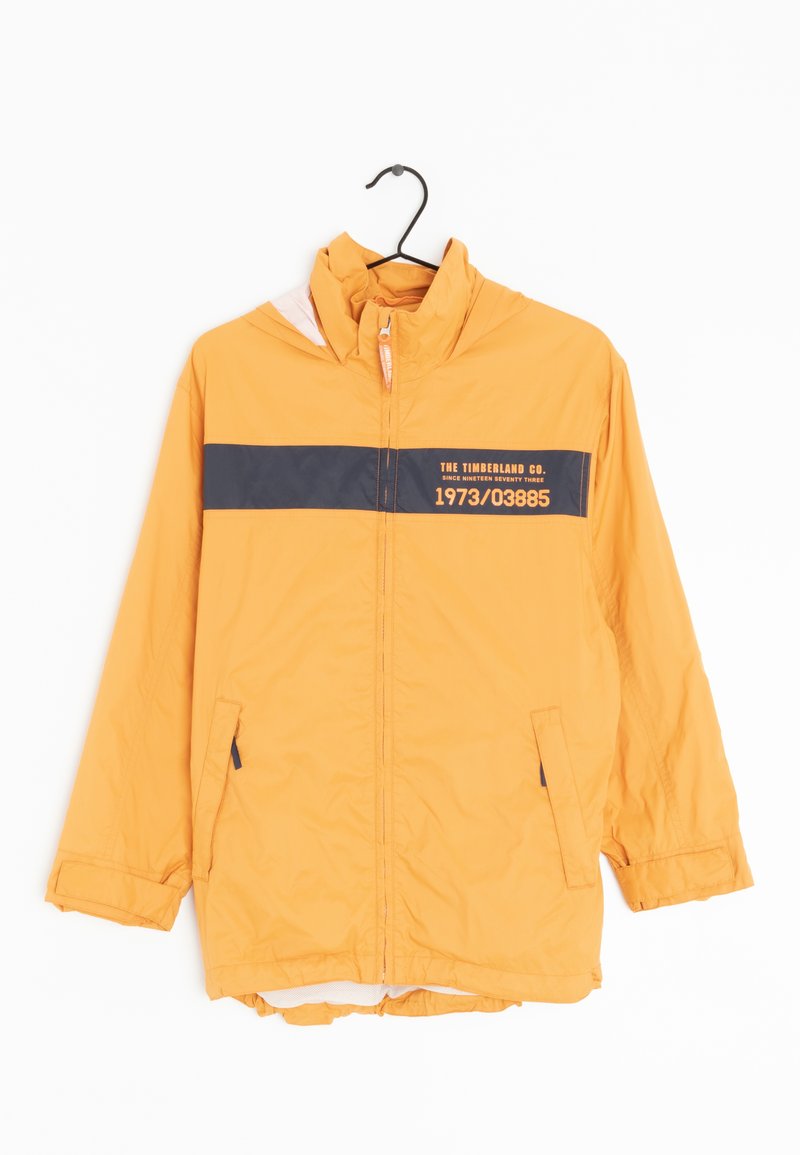 Gul Timberland-jacka med huva, svart horisontell rand och text, dragkedja fram och framfickor, hängande på en svart galge.