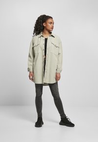 Světle zelená oversized košile-jacket s dvěma náprsními kapsami, zapínání na knoflíky, v kombinaci s černým crop topem a tmavými džíny, stylizováno s černými teniskami.