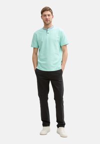 Mintově zelená polo košile s krátkým rukávem a kulatým výstřihem, dvouknoflíkovým zapínáním a tmavě šedými kalhotami. Outfit doplňují tenisky.
