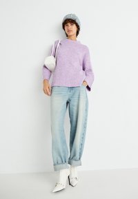 Svijetloplavi pleteni pulover s rebrastim rubom, kombiniran s svijetloplavim širokim trapericama i bijelim špicastim gležnjačama. Bijela torba i sivi kapu.