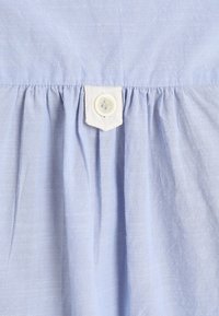 Tissu bleu clair avec des plis froncés et un petit bouton blanc cousu sur une languette rectangulaire.
