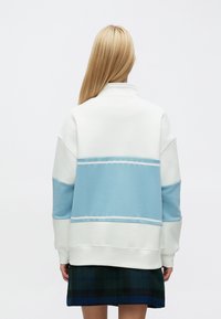 Valge ja helesinise kontrastidega dressipluus kõrge kraega ja pikkade varrukatega, millel on horisontaalsed triibud ja pehme tekstuur.