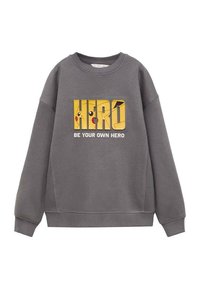 Grijze sweatshirt met een opvallende gele "HERO" grafiek met een cartoonfiguur en de tekst "WEES JE EIGEN HELD." Zacht materiaal en een ontspannen pasvorm.