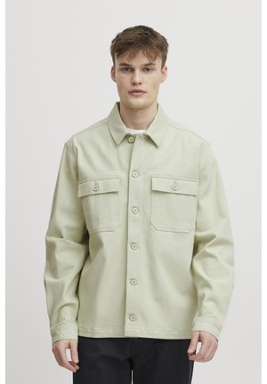 Light green jacket made of cotton, featuring a button-up front, two chest pockets, and a relaxed fit with long sleeves.
