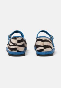 Buty w cętkowy wzór zebry z niebieskim paskiem i wykończeniem, wykonane z teksturowanej tkaniny, z czarną gumową podeszwą i zaokrąglonym kształtem.
