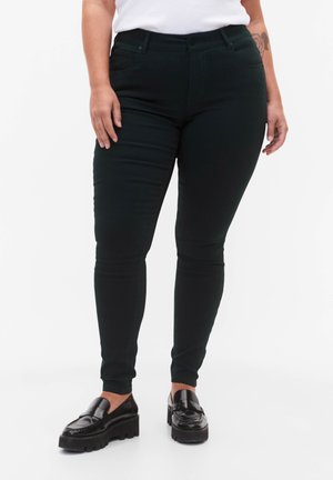 Črne skinny kavbojke z gladko teksturo, ki imajo pet žepov in povprečen pas, v kombinaciji s črnimi masivnimi loaferji.