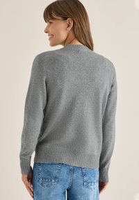 Maglione grigio a maglia con scollatura rotonda, orlo e polsini a costine, visto da dietro. Abbinato a jeans azzurri chiari e strutturati.