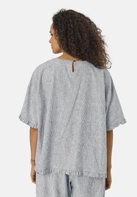 Lätt, blårandig topp med korta ärmar, nyckelhål i ryggen och fransad fåll. Tillverkad av andningsbart tyg, designad för komfort.