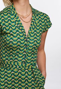 Grön och gul mönstrad plagg med korta ärmar, krage och knappstängning, med en geometrisk design och textil med struktur.