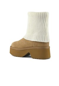 Botas de ante marrón claro con un puño de punto crema acanalado, suela de plataforma gruesa y suela texturizada. Presenta costuras suaves a lo largo de los bordes.