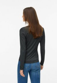 Černá košile s dlouhým rukávem a slim fit, vyrobená z texturované tkaniny s jemnými metalickými pruhy, spárovaná s modrými džínami s vysokým pasem.