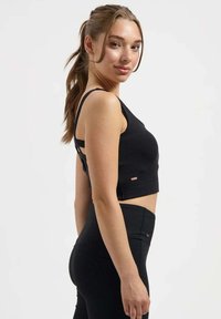 Schwarzes, kurzes Tanktop mit schmalen Trägern, figurbetontem Design und strukturierter Stoff. Der Rücken ist mit ausgeschnittenen Details und einem kleinen Logoakzent versehen.