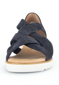 Donkerblauwe suède sandaal met gekruiste banden, een natuurlijke leren inlegzool en een witte rubberen zool met een gestructureerd patroon.