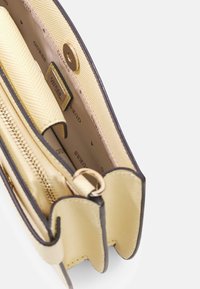 Borsa sintetica gialla con texture e rifinitura marrone; presenta una tasca con cerniera e una chiusura con bottone a scatto. Interno con fodera brandizzata.