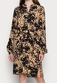 Leopardmönstrad skjortklänning i tan och svart, med långa ärmar, knapplist, knytning i midjan och slits på sidan för extra rörelse. Mjukt tyg.