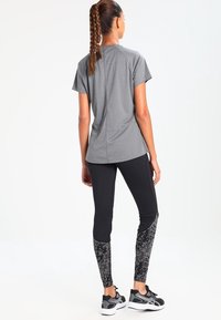Camiseta atlética gris de manga corta, combinada con leggings negros que tienen un diseño texturizado en la parte inferior de las piernas. Zapatillas deportivas negras.